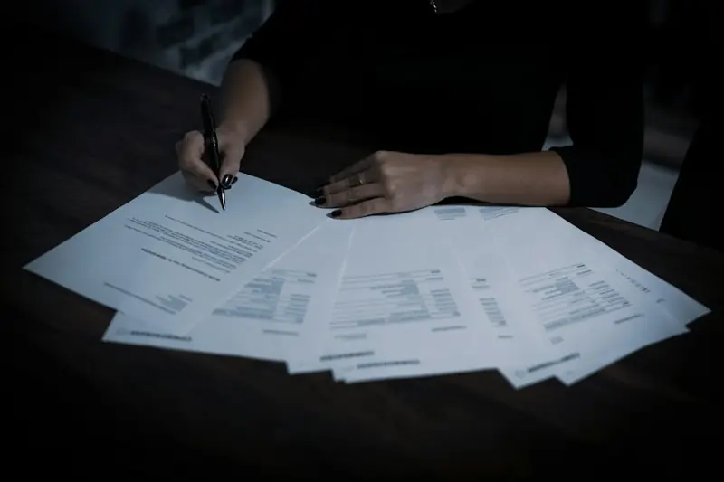 Manos firmando documentos sobre una mesa oscura